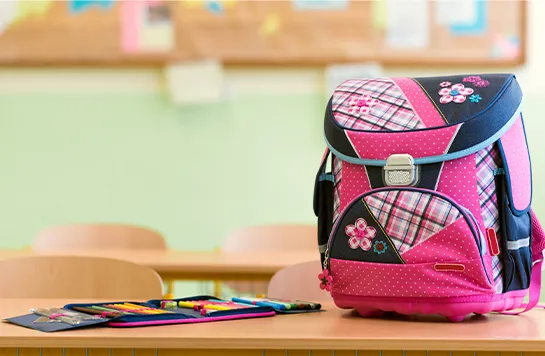 Ein pinker Schulranzen mit Federmäppchen steht auf einem Tisch in einem Klassenzimmer.