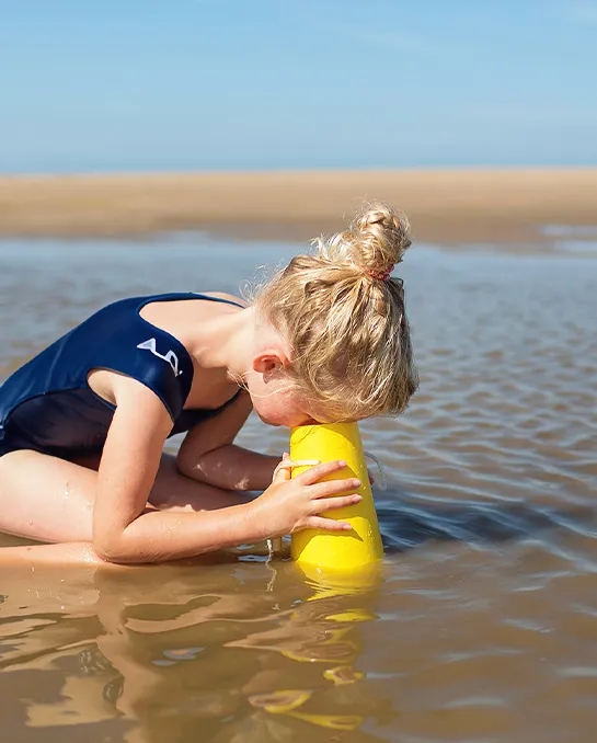 Kind sitzt im Wasser und benutzt eine Unterwasserlupe