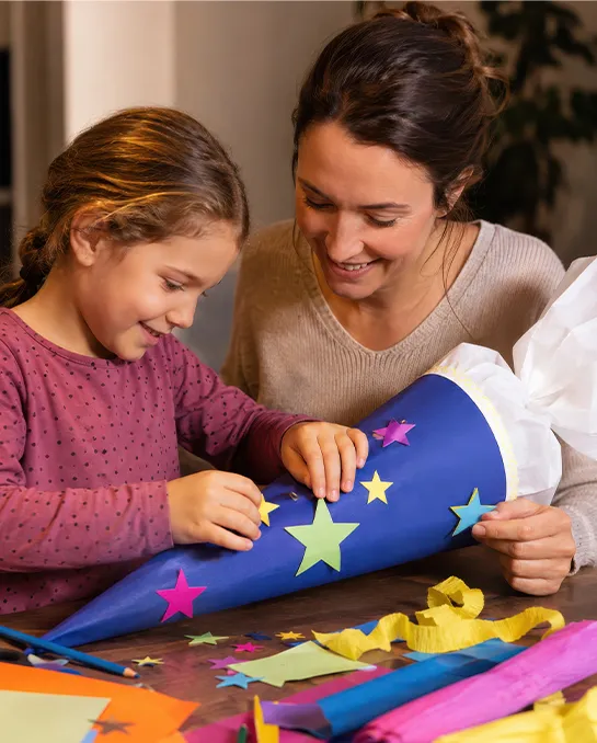 Mutter und Mädchen basteln gemeinsam an einer blauen Schultüte mit Sternen
