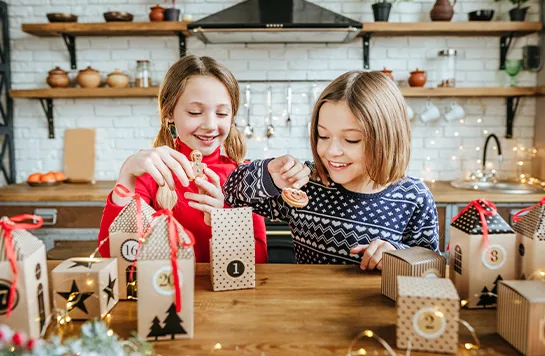 Zwei Mädchen öffnen gemeinsam kleine weihnachtliche Adventskalender Päckchen